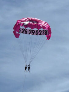 Two parasail flyers in the air under a pink umbrella